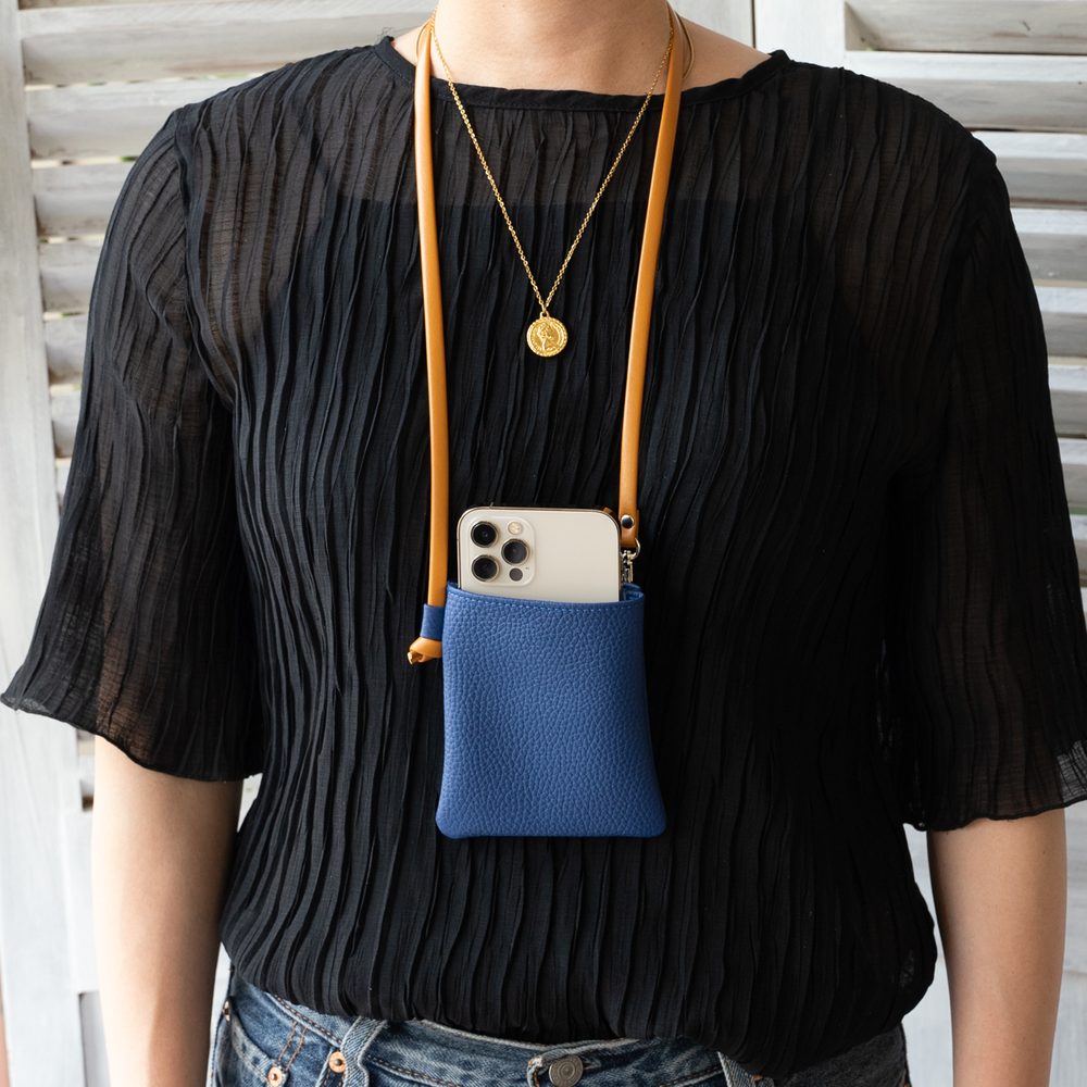 黒い服の女性が本革ネックポーチ ロイヤルブルーを首から下げ、iPhoneのカメラが前を向いている着用イメージ